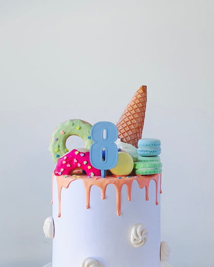 A colorful cake topped with an ice cream cone, macarons, and a number 8 candle.