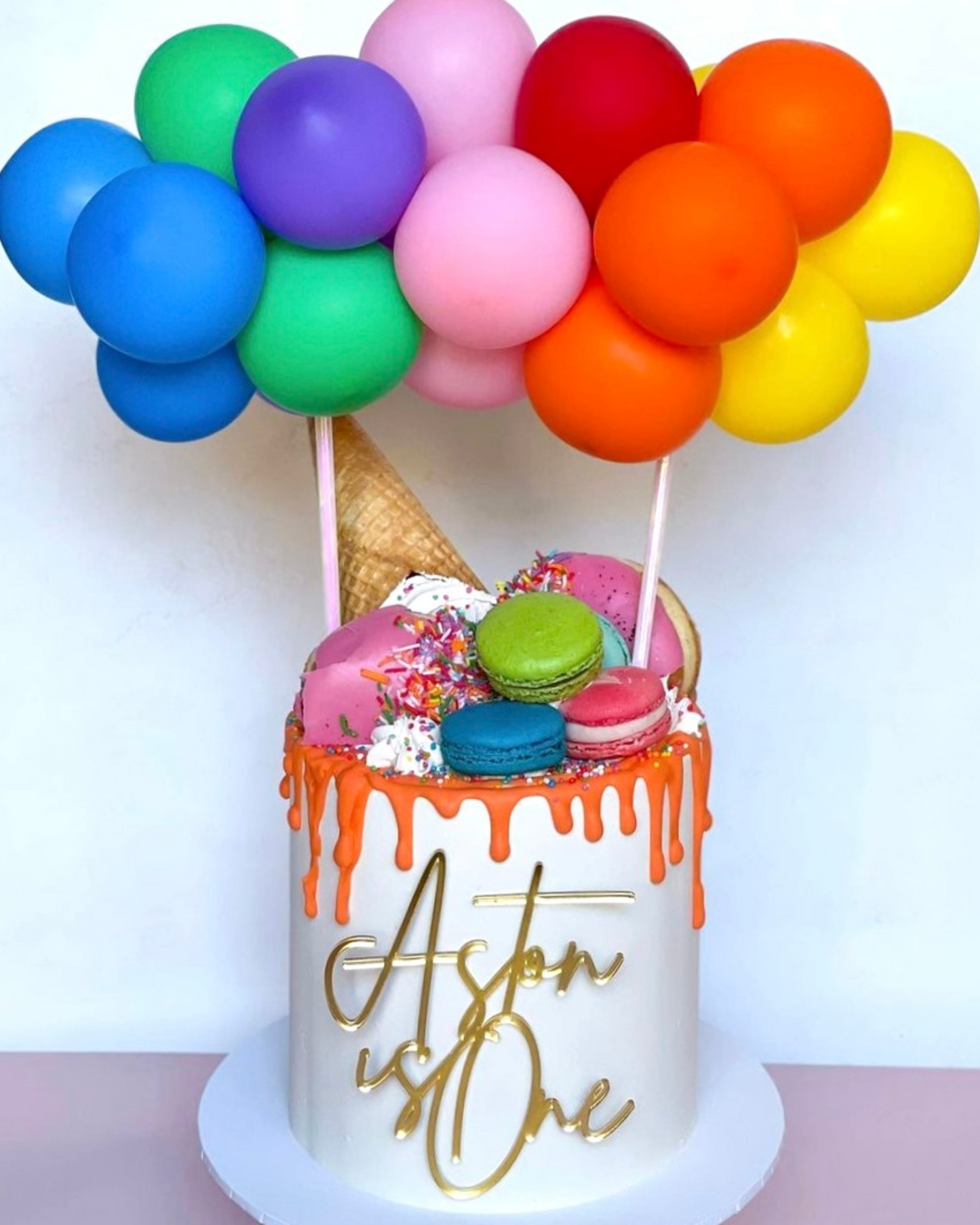 Colorful balloons float above a vibrant cake topped with macaroons and sprinkles, celebrating a special occasion.