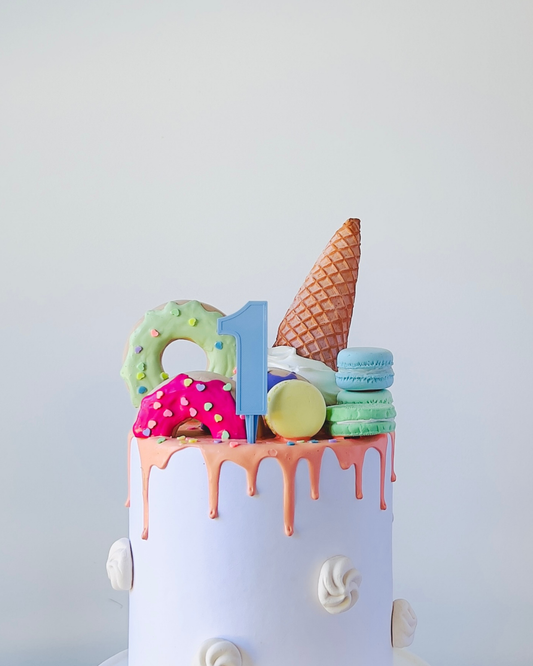 A whimsical cake topped with colorful treats, featuring a blue number one and dripping icing. Perfect for a celebration.