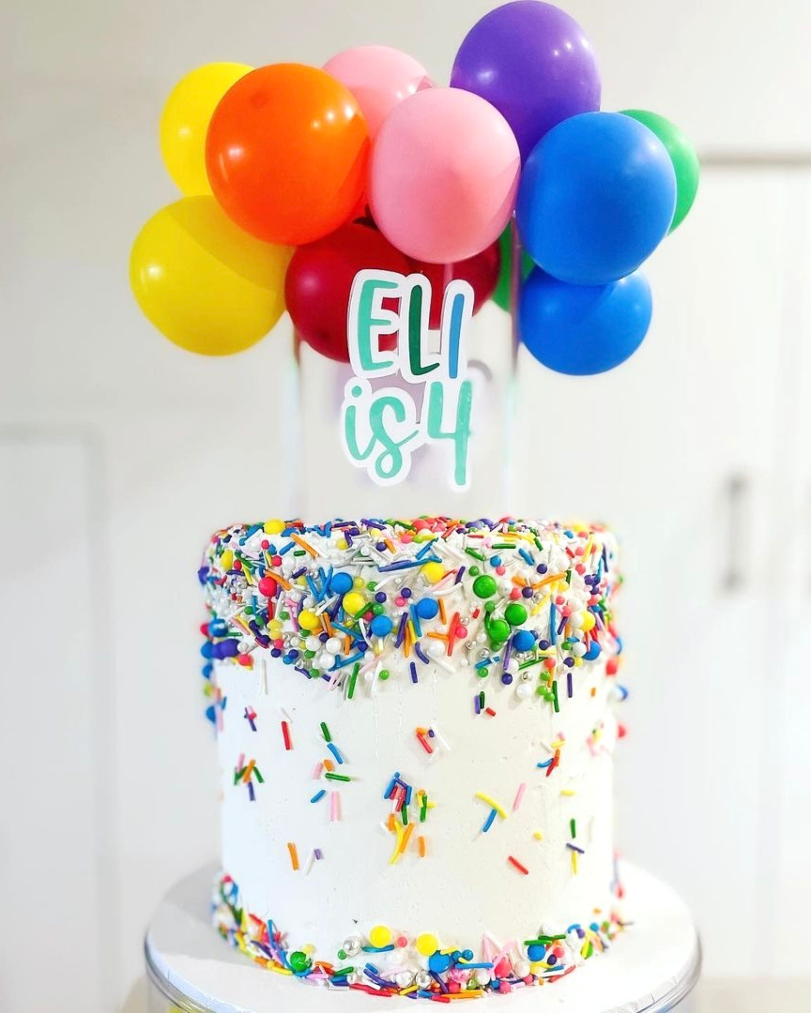 A colorful cake topped with balloons and festive sprinkles, celebrating a fourth birthday.