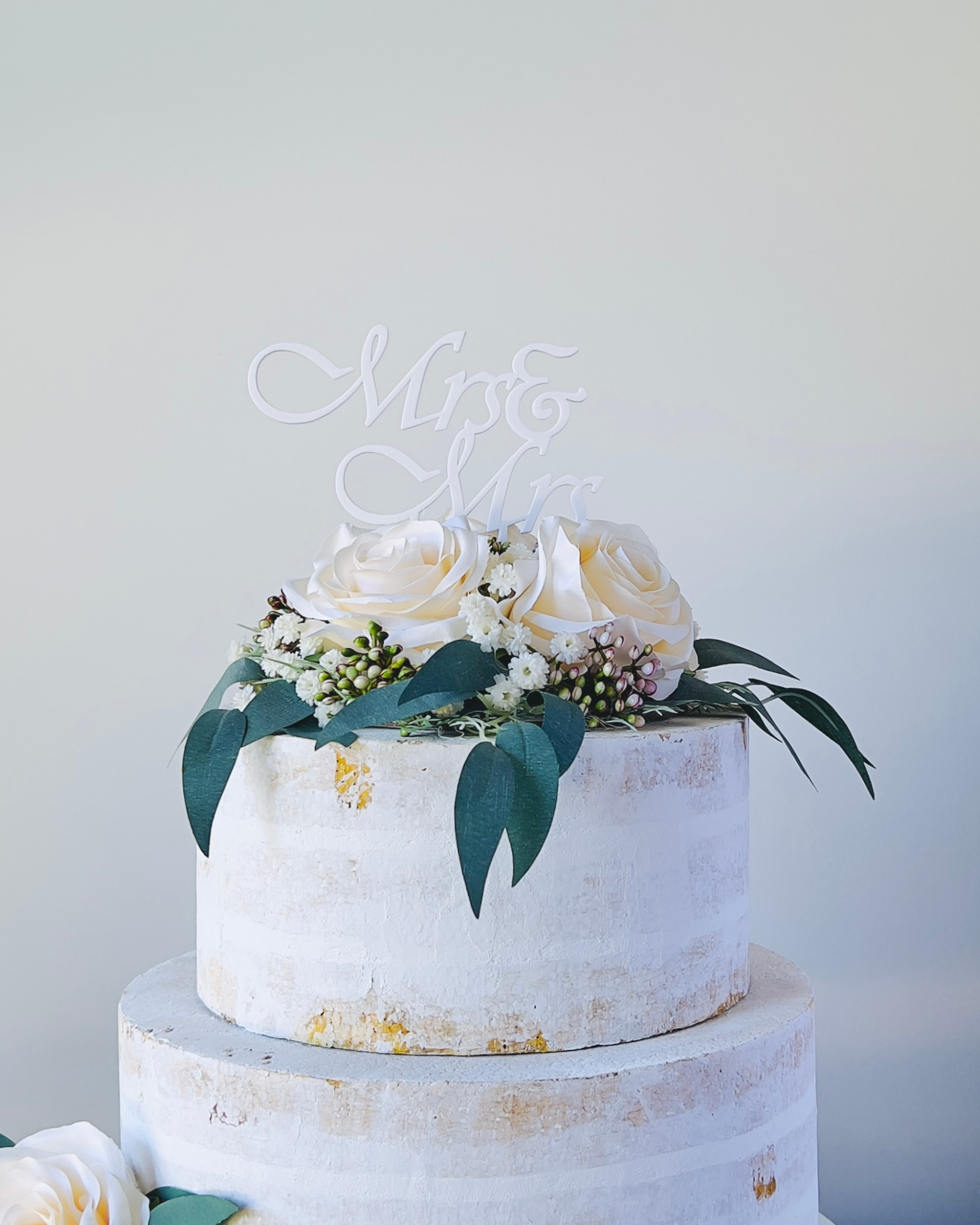 A tiered arrangement featuring white roses, greenery, and a decorative "Mr & Mrs" sign on top.