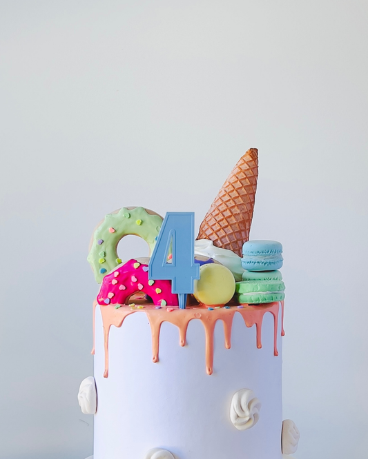 A colorful cake topped with playful sweets, a number four, and a waffle cone, all against a minimalist backdrop.