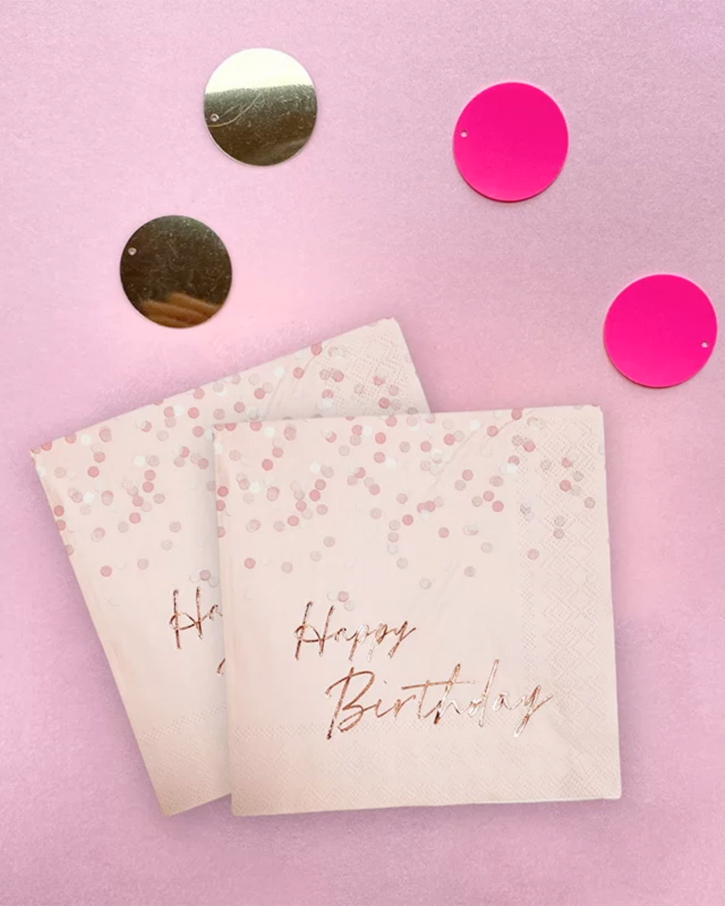 Two pink napkins with "Happy Birthday" in rose gold, surrounded by shiny gold and bright pink circles on a soft background.