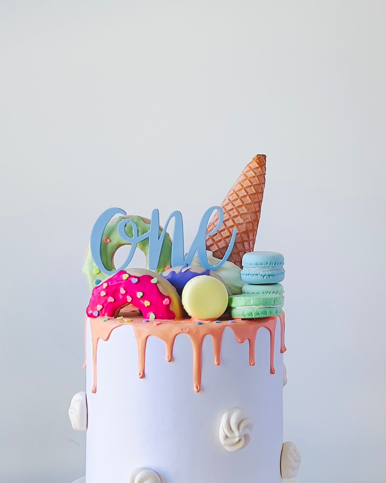 Colorful cake topped with a cone, macarons, and playful decorations, celebrating a first birthday.