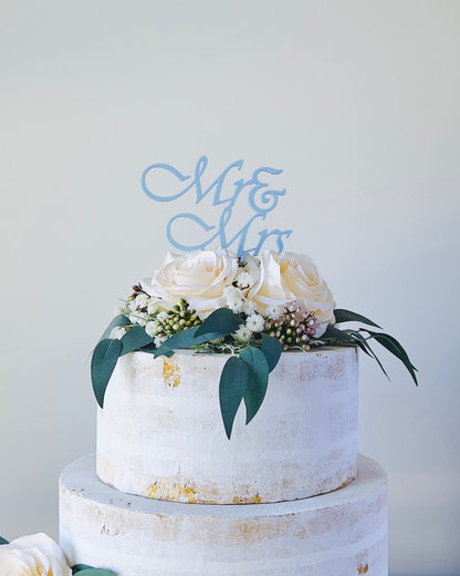 A tiered display featuring white roses, greenery, and a light blue "Mr. & Mr." topper against a soft background.