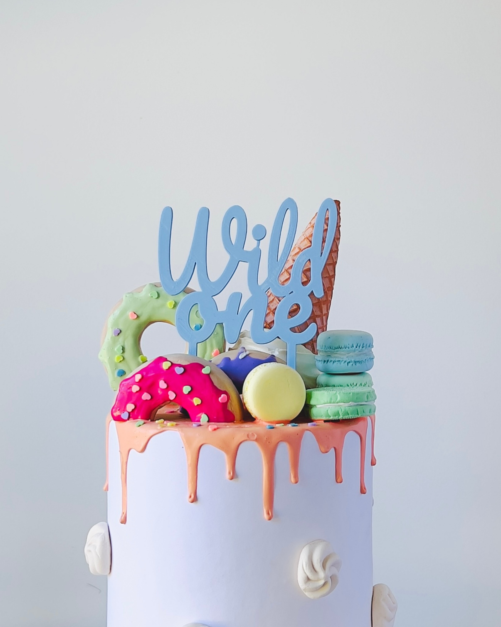 Colorful confections topped with a blue "Wild One" sign, featuring donuts, macarons, and an ice cream cone.