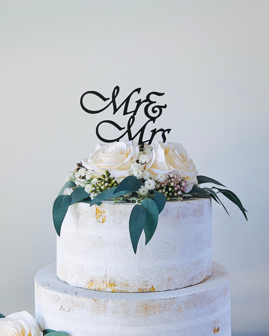 A tiered display featuring white roses and greenery, topped with a stylish "Mr & Mr" sign against a light background.