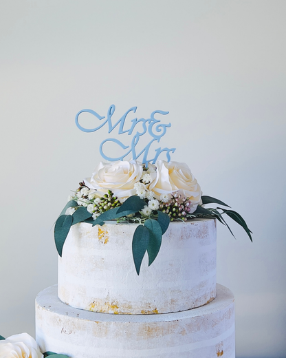 A two-tiered display topped with white roses, greenery, and a blue "Mr & Mrs" sign against a soft background.