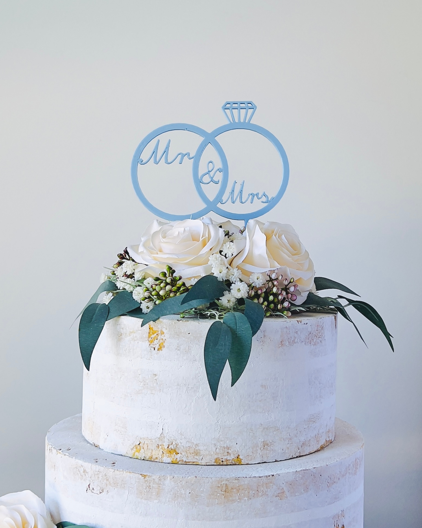 A decorative cake topper featuring interlocking rings and floral accents, ideal for a wedding celebration.