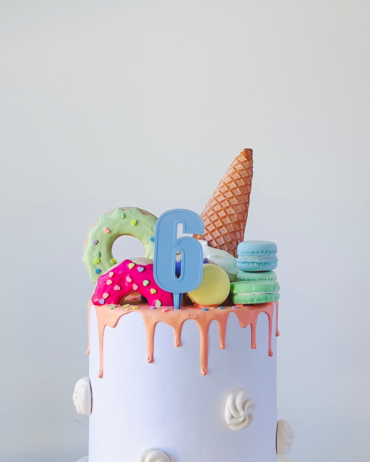 A colorful cake topped with a number six, ice cream cone, and assorted decorated treats.