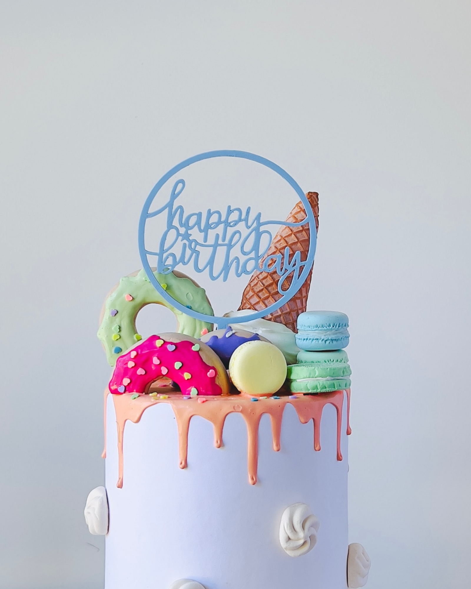 Colorful cake topped with playful sweets and a festive "Happy Birthday" sign in a light and cheerful setting.