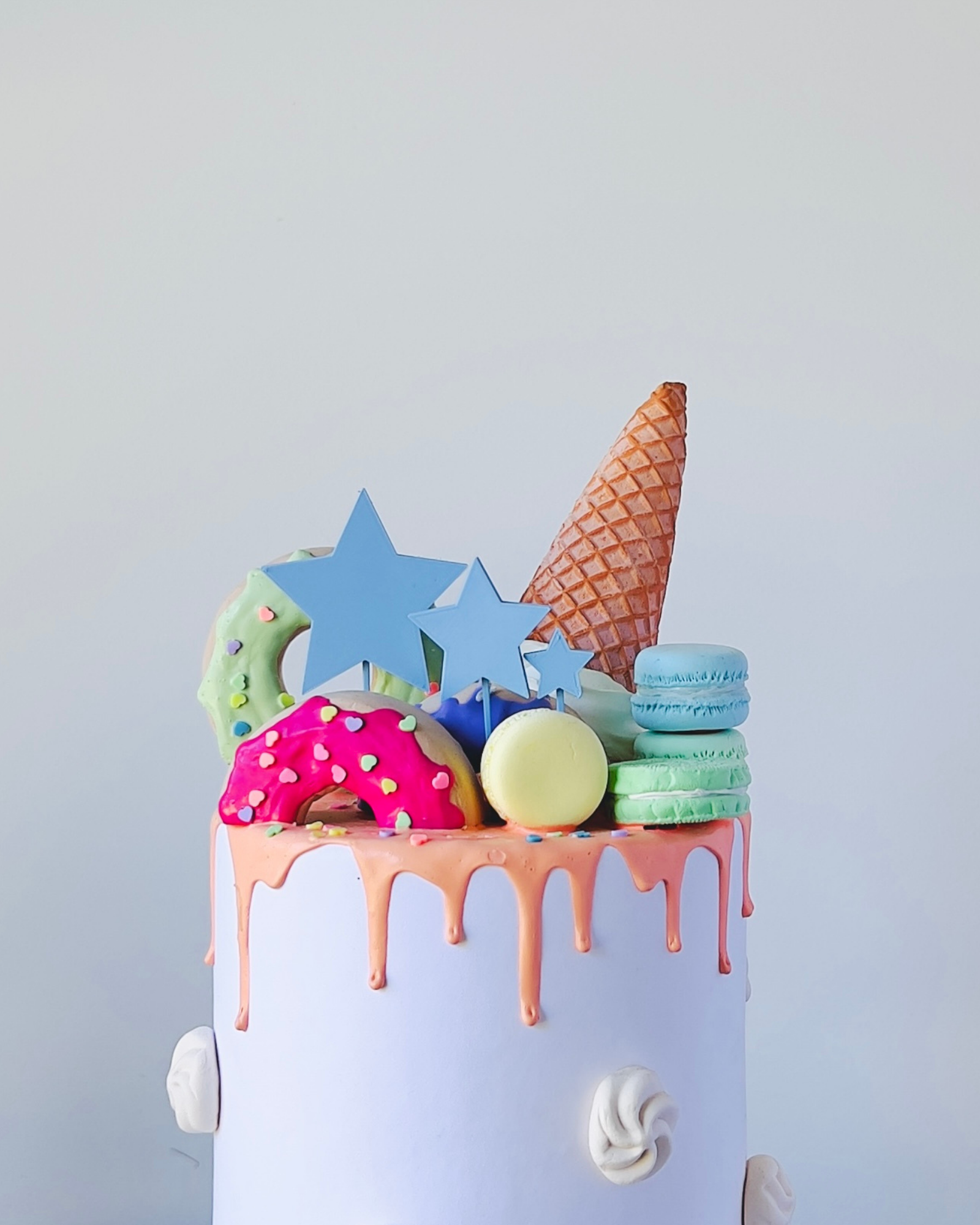 A colorful confection topped with stars, ice cream cone, and various decorated sweets, drizzled with vibrant icing.