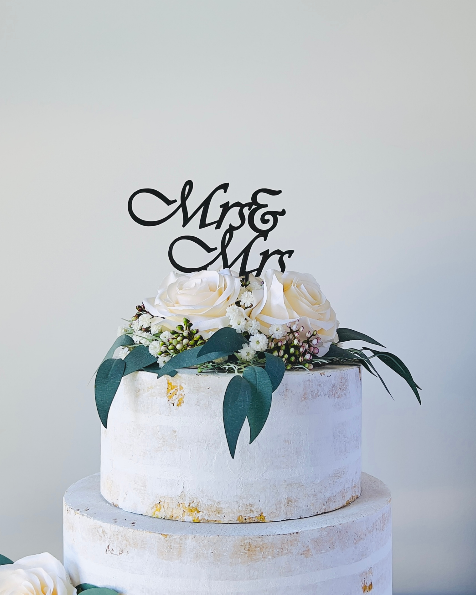 A tiered display topped with white roses and greenery, featuring a decorative "Mr & Mr" sign.