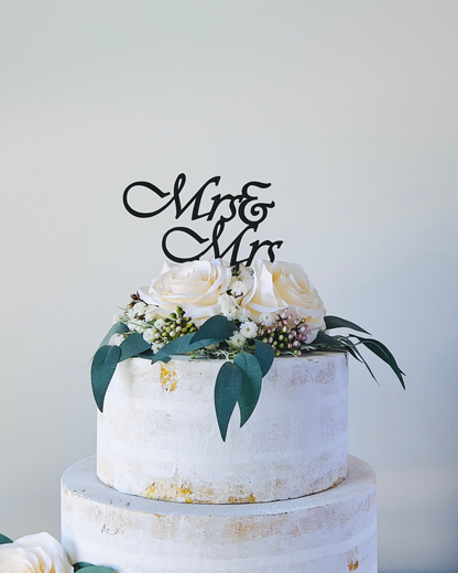 A tiered display topped with white roses and greenery, featuring a decorative "Mr & Mr" sign.