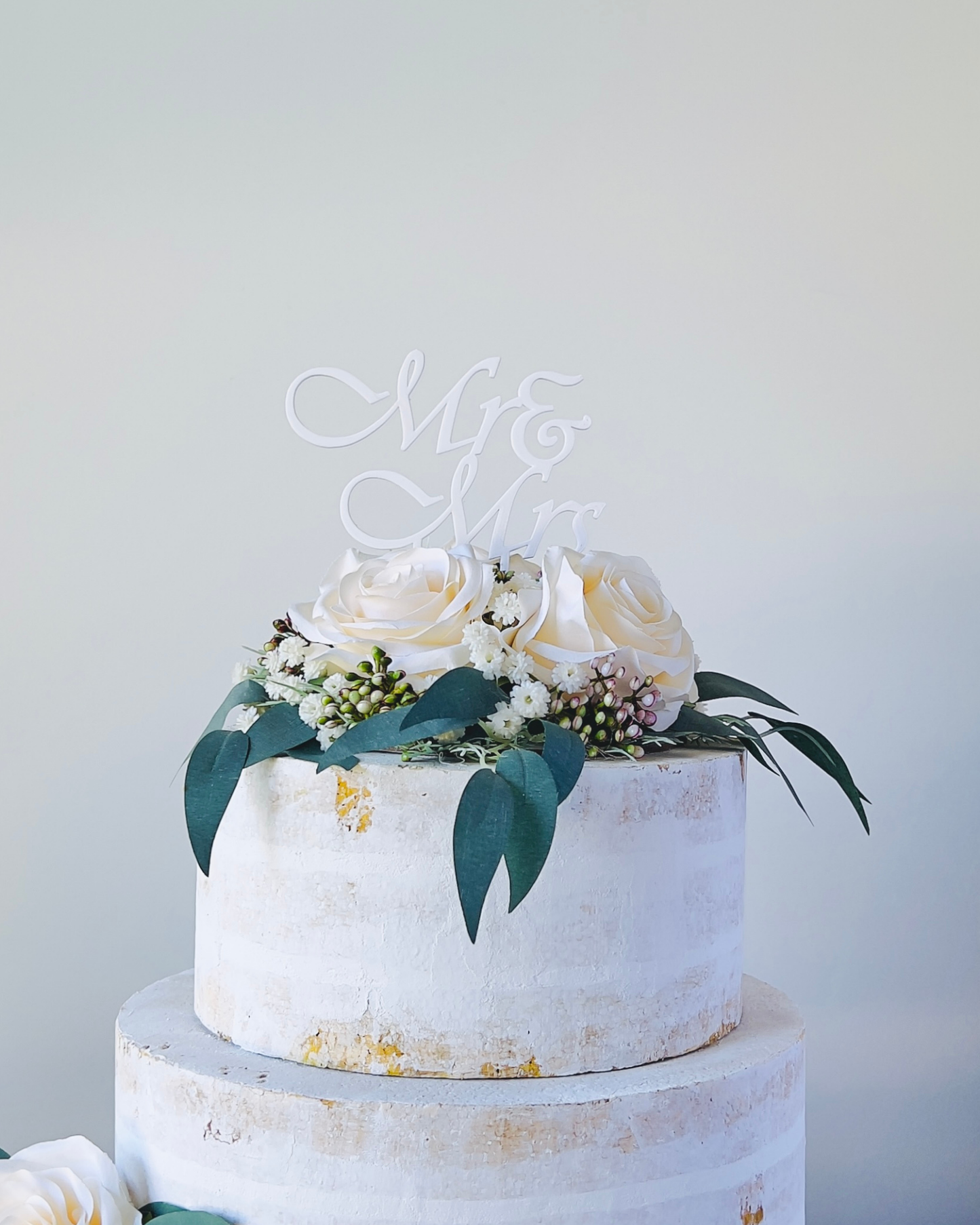 A decorative three-tiered arrangement topped with white roses and greenery, featuring a "Mr & Mr" sign.