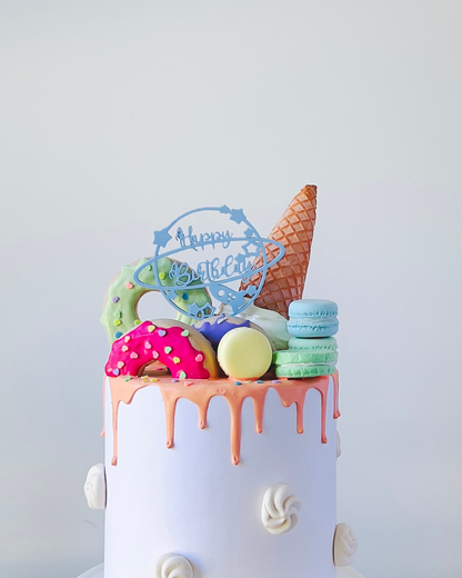 A colorful cake topped with playful sweets and a "Happy Birthday" decoration against a light background.