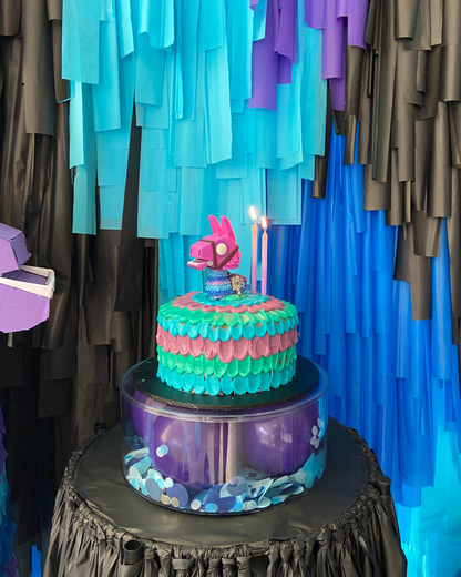 A colorful cake with a pinata topper and candles, set against a vibrant backdrop of layered blue and black decorations.