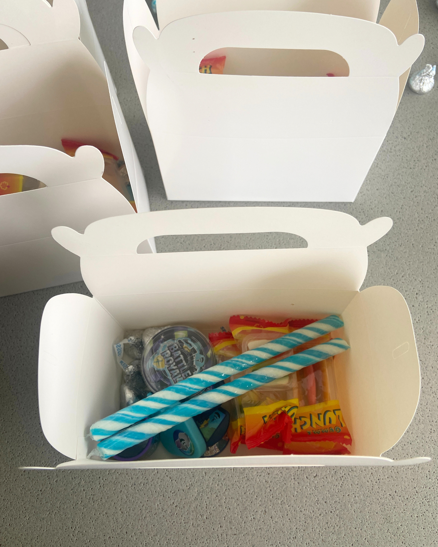 Open white container filled with colorful candies and treats, featuring two blue and white striped sticks on top.