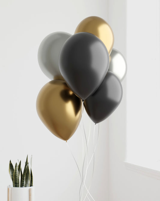 A cluster of glossy black, silver, and gold balloons against a light background, with delicate white strings.