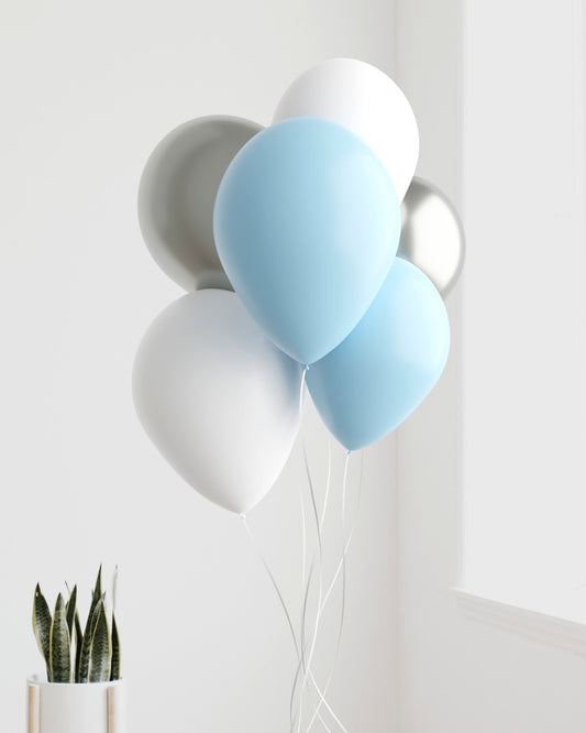 A cluster of blue, white, and silver balloons with long white strings, near a potted plant against a light background.