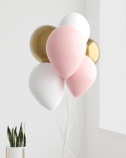 A cluster of pink, white, and gold balloons against a light background, with green leaves in a pot nearby.