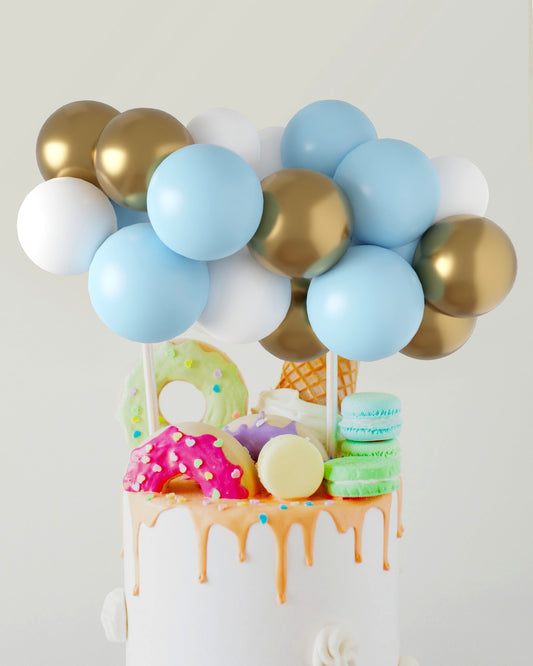 Colorful balloons in blue, white, and gold atop a cake adorned with vibrant sweets and dripping icing.