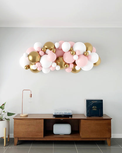 A vibrant garland of pink, white, and gold balloons decorates a modern wall above a wooden console table.