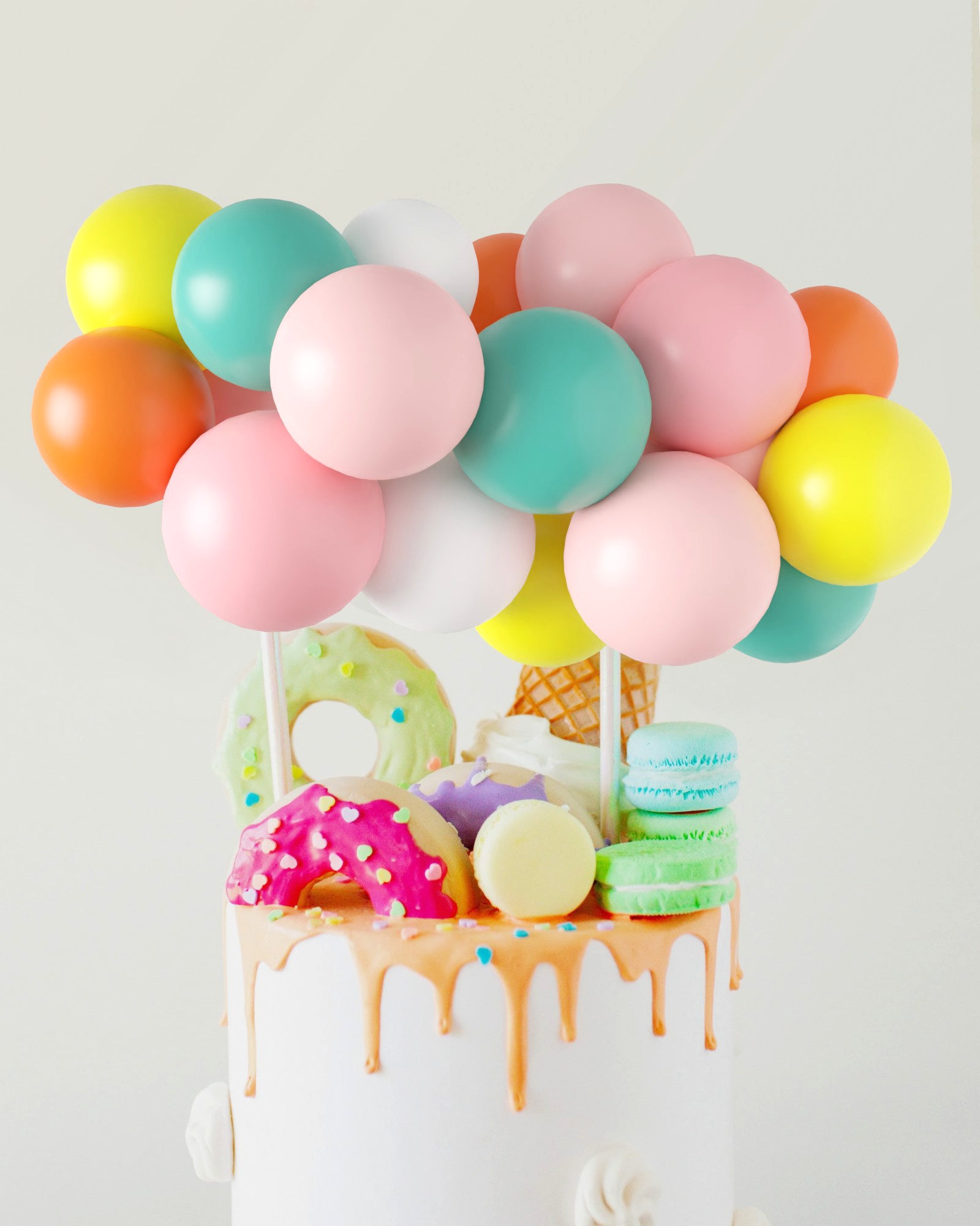 A colorful balloon cluster atop a cake adorned with donuts, macarons, and an ice cream cone, dripping with frosting.