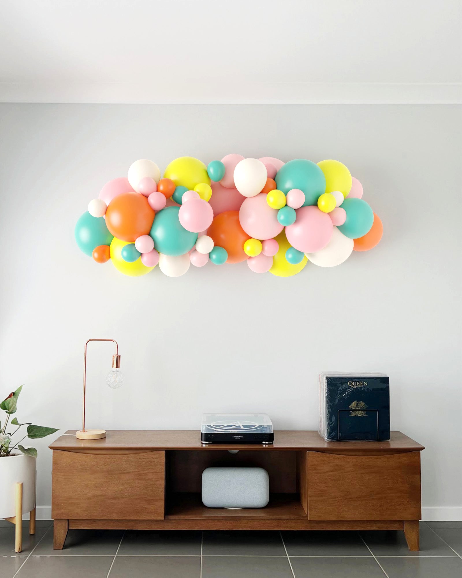 A vibrant balloon garland in pastel colors decorates a light wall above a stylish wooden console table.