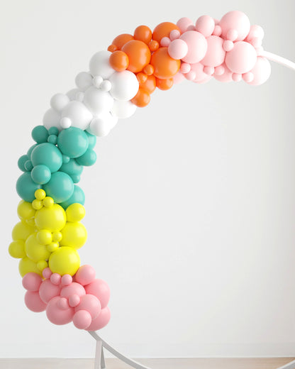 Colorful balloon garland in shades of pink, orange, green, yellow, and white, arching gracefully against a light background.