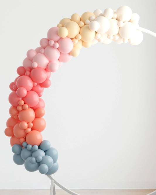 Colorful balloon arch featuring shades of pink, peach, yellow, and blue against a light background.