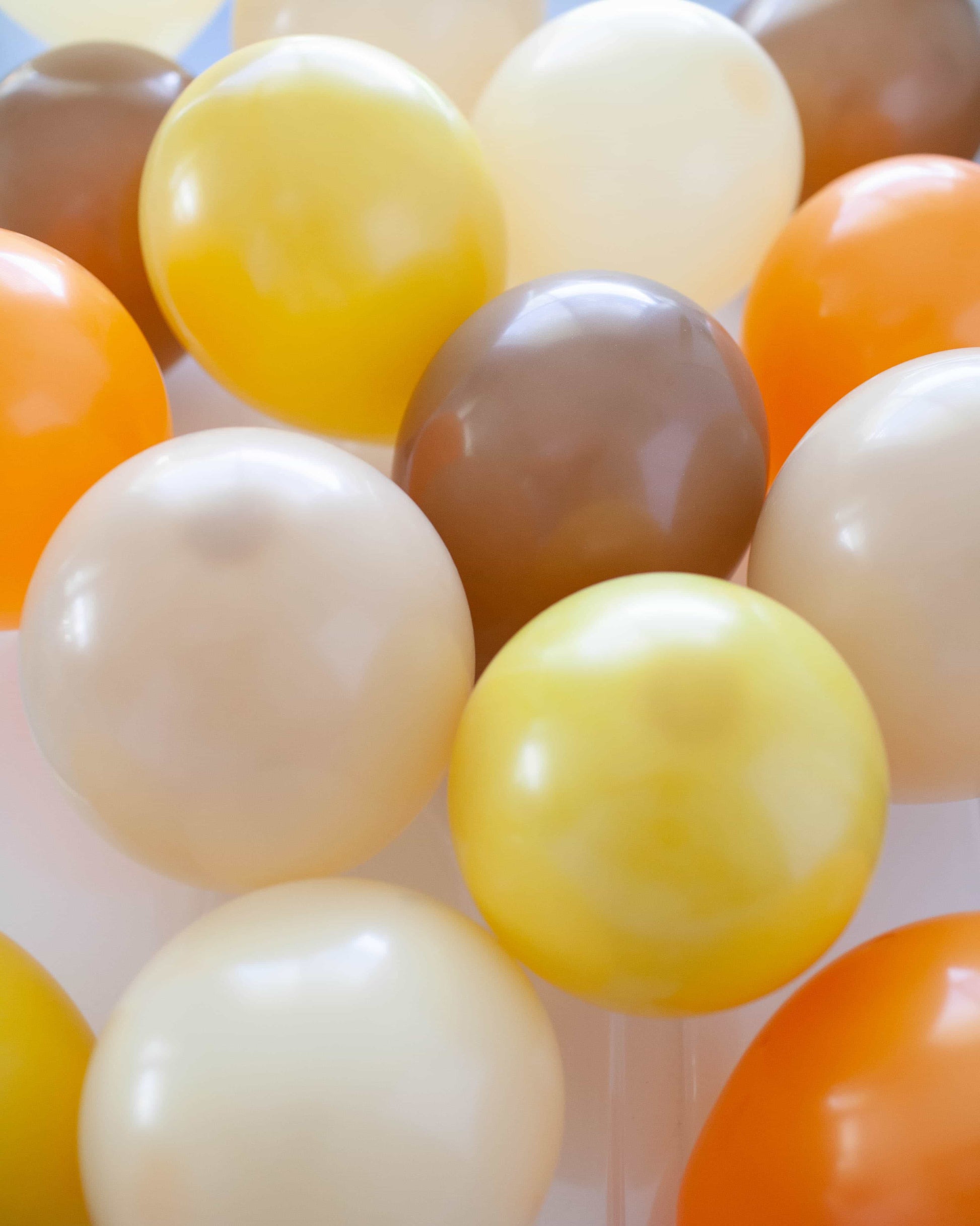 A cluster of colorful balloons in shades of yellow, orange, brown, and cream, creating a vibrant, festive atmosphere.