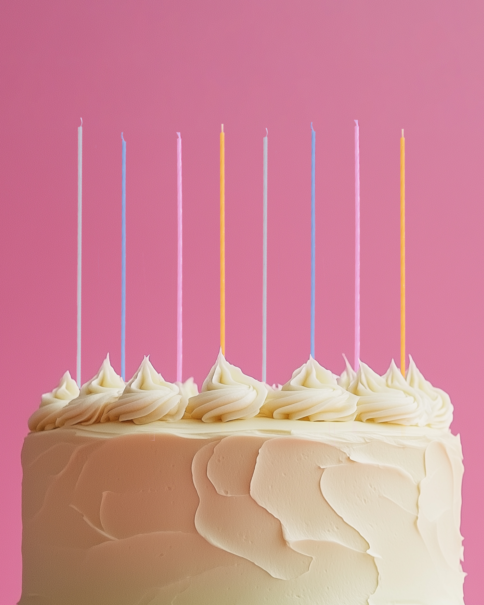 A pastel cake topped with swirls of icing and colorful candles against a vibrant pink backdrop.