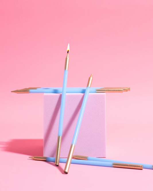 Four blue candles with gold tips arranged around a soft pink block against a vibrant pink background.