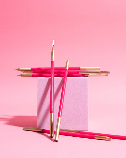 Bright pink candles with gold tips arranged on a pastel pink block against a matching background, creating a festive look.