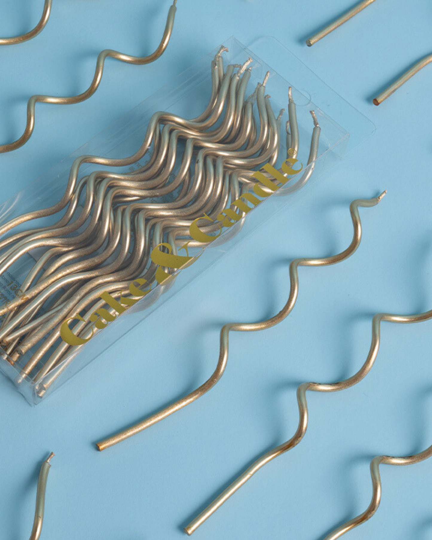 Gold wavy candles arranged over a light blue background, with a transparent pack partially visible.