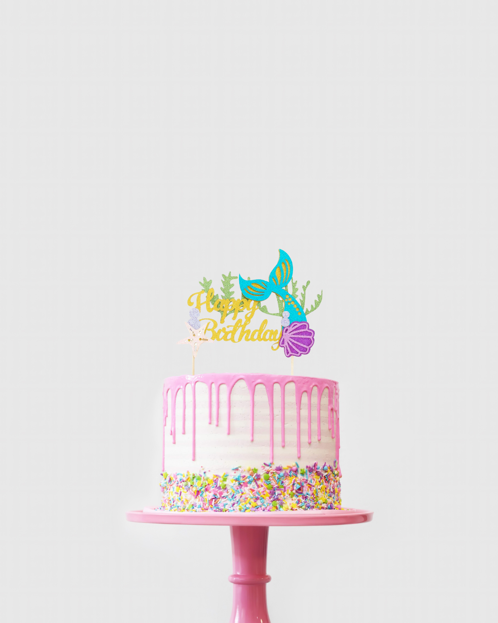 A colorful birthday cake with pink icing, dripping glaze, and a vibrant mermaid-themed topper.