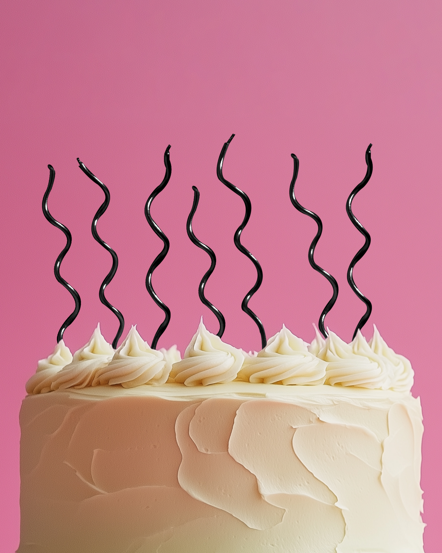 A frosted cake topped with spiraled black candles against a vibrant pink background.