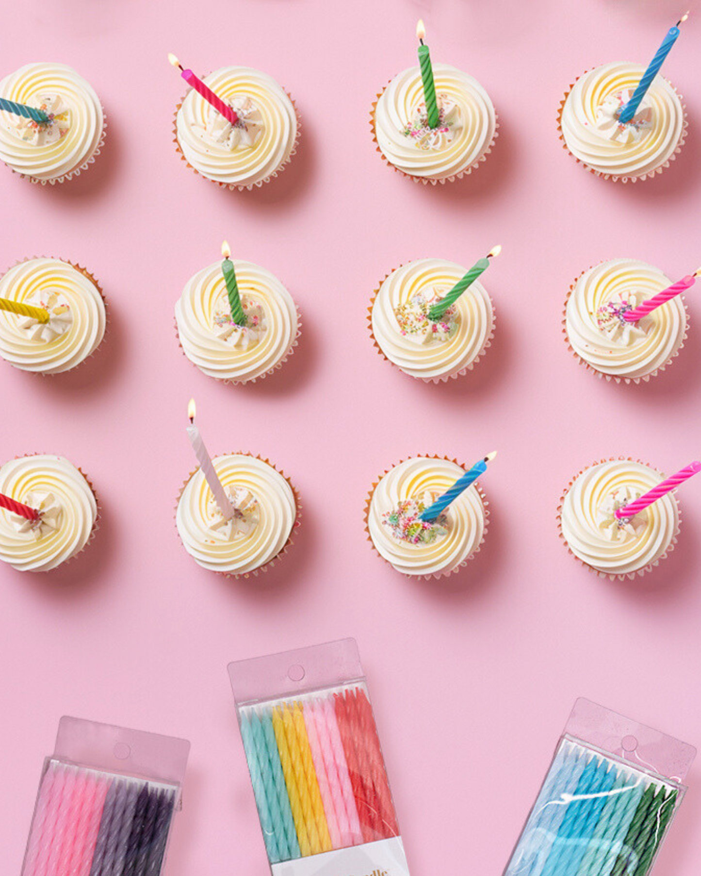 Colorful candles on frosted cupcakes arranged on a pink background, adding a festive touch to the scene.