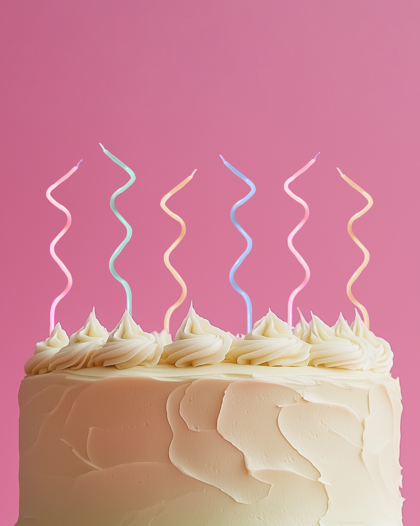 A pastel-colored cake topped with swirled frosting and vibrant, spiraled candles against a soft pink backdrop.