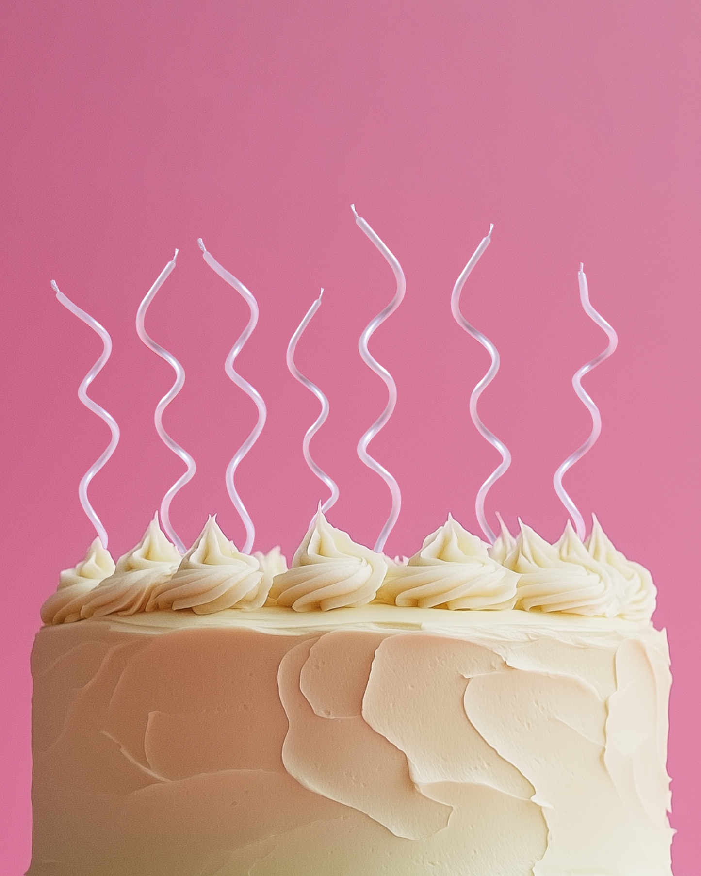 A frosted cake with swirled pink candles on top, set against a bright pink background.