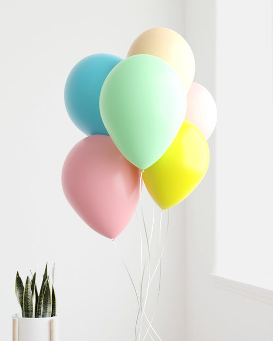 A cluster of colorful balloons in pastel shades with a potted plant nearby, brightening a serene indoor space.