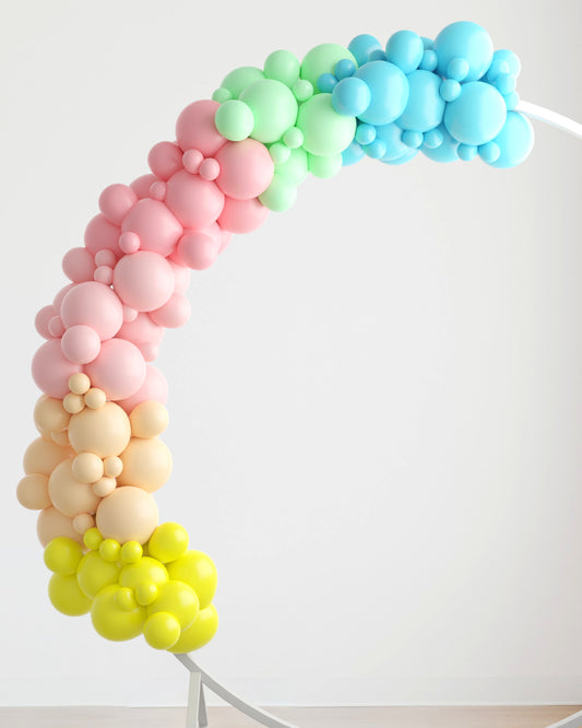 A colorful arch made of pastel balloons in shades of pink, green, blue, and yellow against a light background.