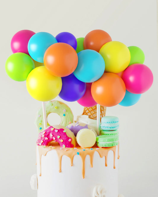 Colorful balloons in vibrant hues atop a cake adorned with playful sweets like donuts, macarons, and an ice cream cone.