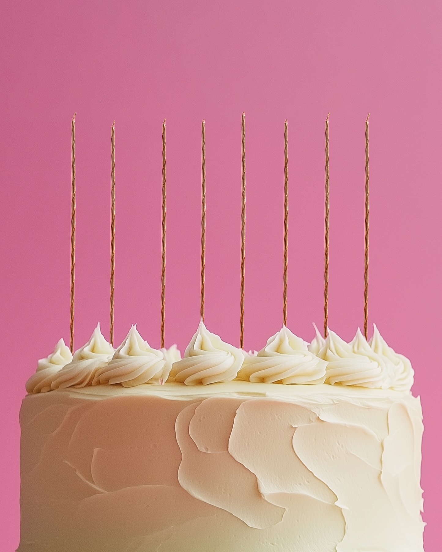 A tall cake with swirled cream frosting topped with golden spiral candles against a vibrant pink background.