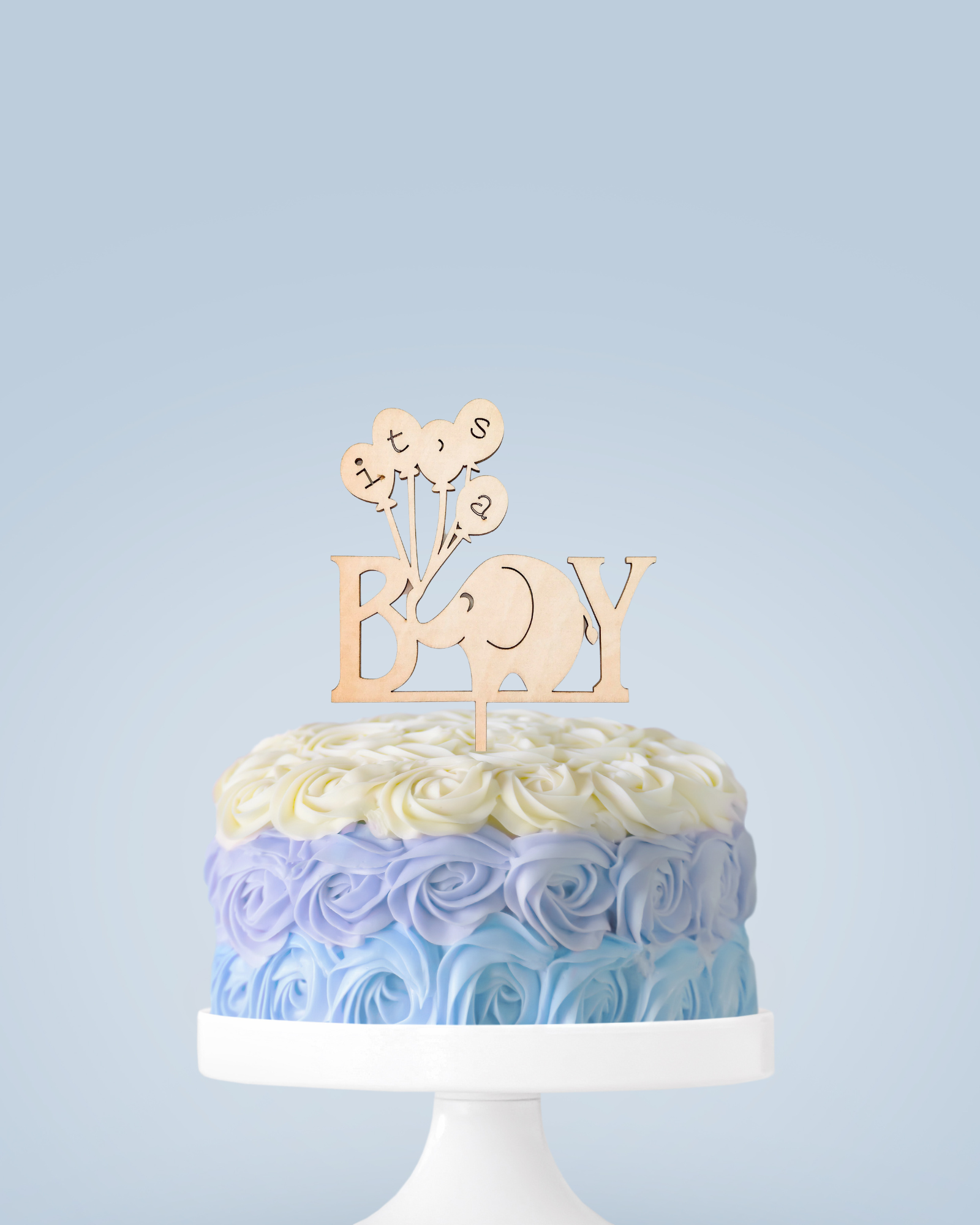 A pastel-colored cake with rose decorations, topped with a wooden "It's a Boy" elephant-themed cake topper.