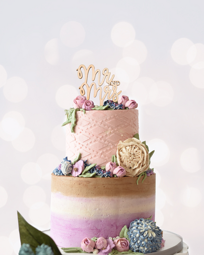 Three-tiered cake adorned with pastel flowers and a "Mr. and Mrs." topper, set against a blurred background.