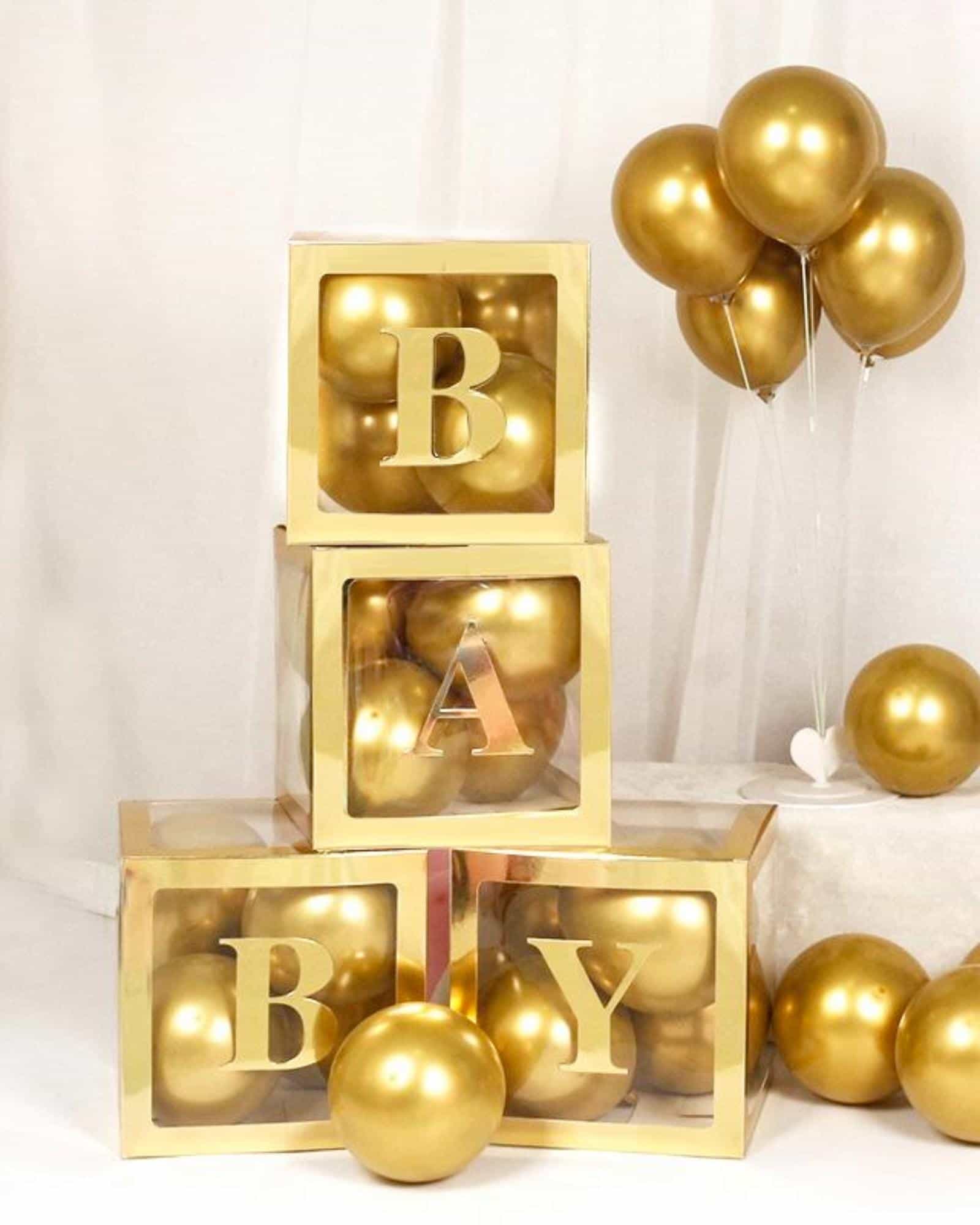 Three golden blocks with letters B, A, and Y, surrounded by shiny gold spheres and a cluster of golden balloons.