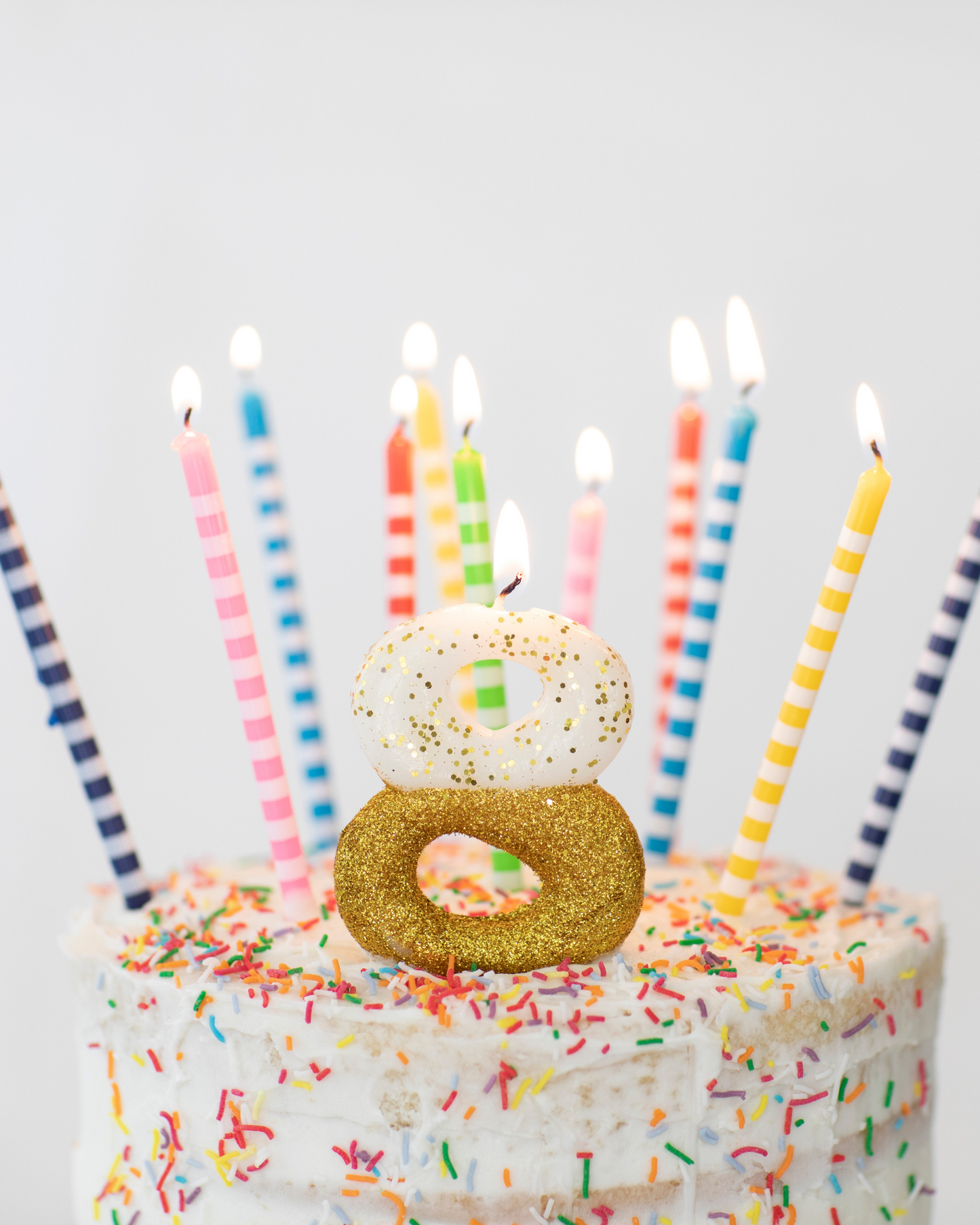 A decorated cake topped with colorful candles and a sparkling number eight, surrounded by vibrant sprinkles.