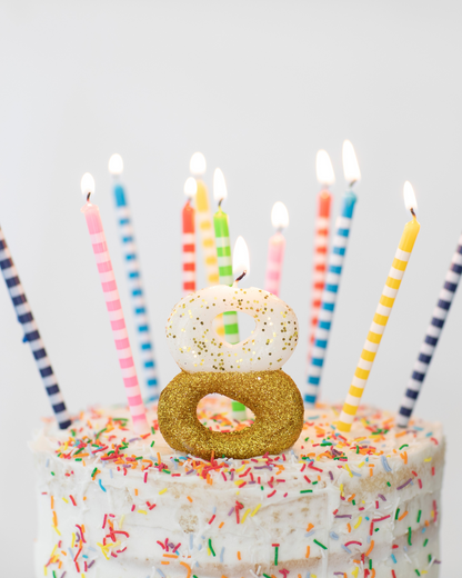 A decorated cake topped with colorful candles and a sparkling number eight, surrounded by vibrant sprinkles.